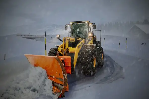 Chargeuse sur pneus équipée d’une lame chasse-neige déneigeant une route enneigée